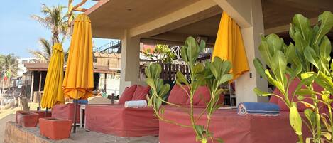 A beachfront seating area with red cushioned benches and yellow umbrellas.