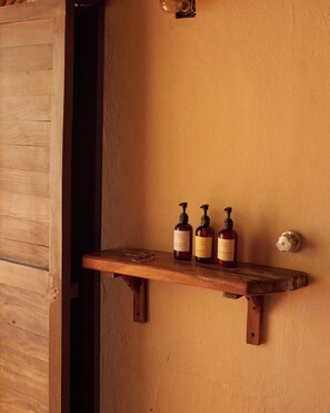 A wooden shelf with three bottles of liquid soap and a metal door handle against a textured wall.