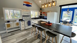 A modern kitchen with a large island, white cabinetry, and a view of the outdoors. - Creekside Cottage - Waterfront Retreat with Kayaks, Fishing & Game Room (Kingsville)