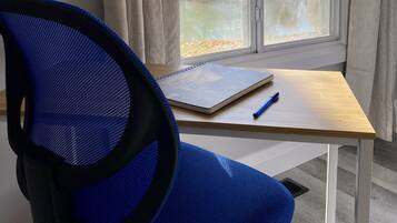 A room with a desk, a chair, a window with a view of trees, and a curtain.