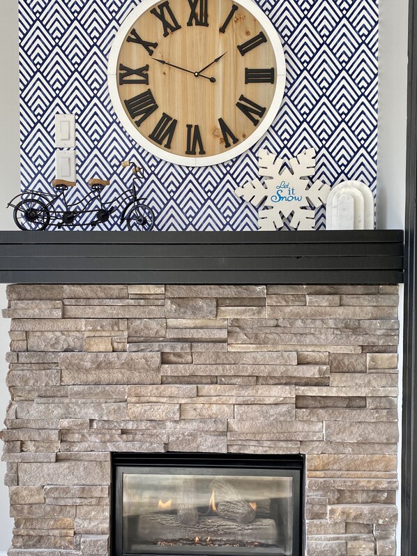 A fireplace with a stone facade, a clock with Roman numerals, and a patterned wall.