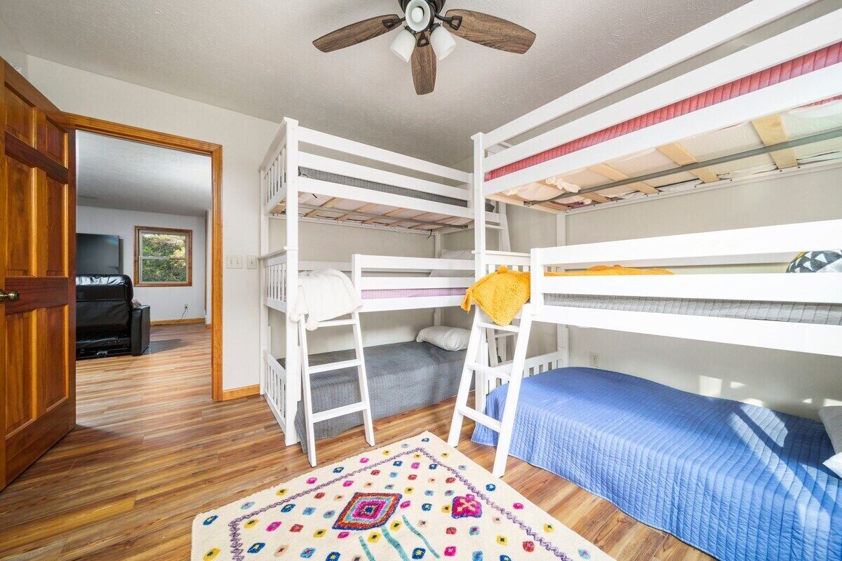 Une chambre avec un lit superposé, un ventilateur de plafond, un plancher en bois et un tapis à motifs.