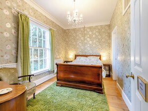 Une chambre à coucher avec un lit en bois, des rideaux verts, un papier peint à motifs floraux, un lustre et un tapis vert.