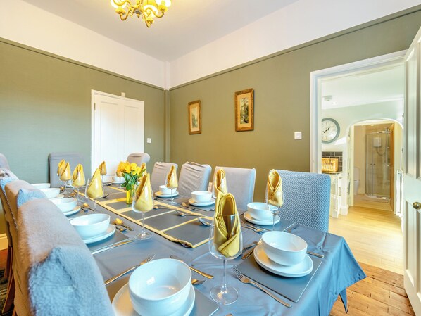 Une salle à manger avec une table dressée pour six personnes, des chaises, un lustre et une porte donnant sur une salle de bain.