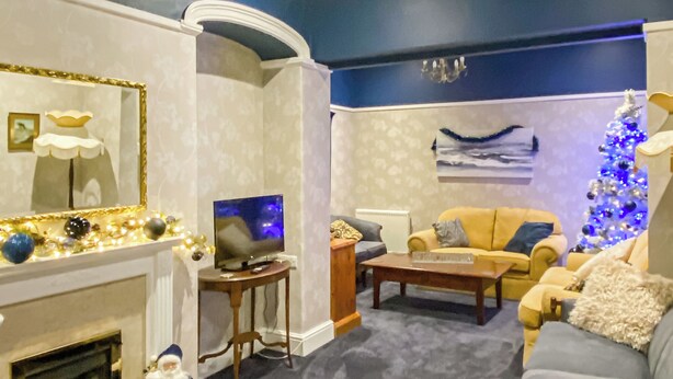 A living room with a fireplace, a television on a stand, a sofa, a Christmas tree, and a painting on the wall. - 5 bedroom accommodation in Wem, near Shrewsbury (Wem, near Shrewsbury)