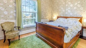 A bedroom with a wooden bed, a chair, a window with curtains, and floral wallpaper. - 5 bedroom accommodation in Wem, near Shrewsbury (Wem, near Shrewsbury)