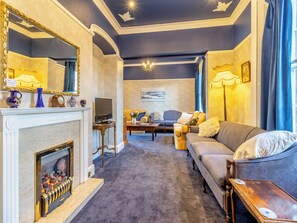 Un salon avec une cheminée, un canapé, un téléviseur et un lustre.