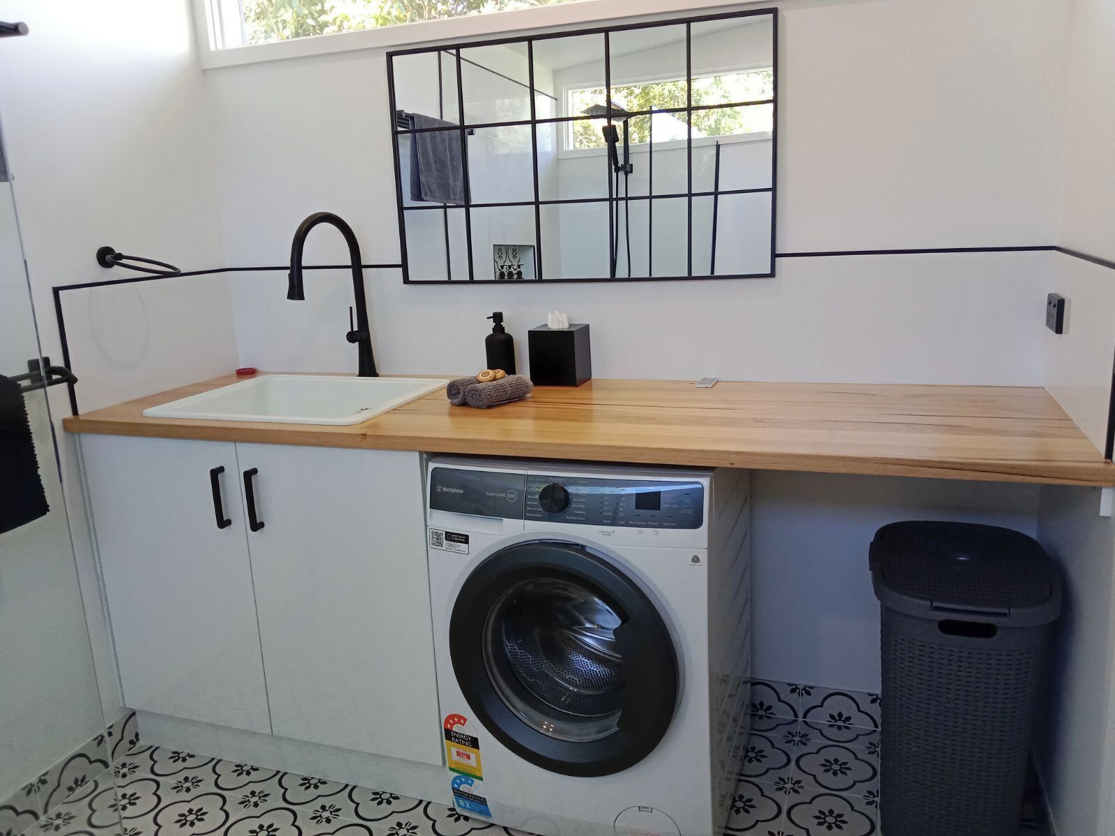 A compact laundry room with a washing machine, a sink, and a mirror above the sink.