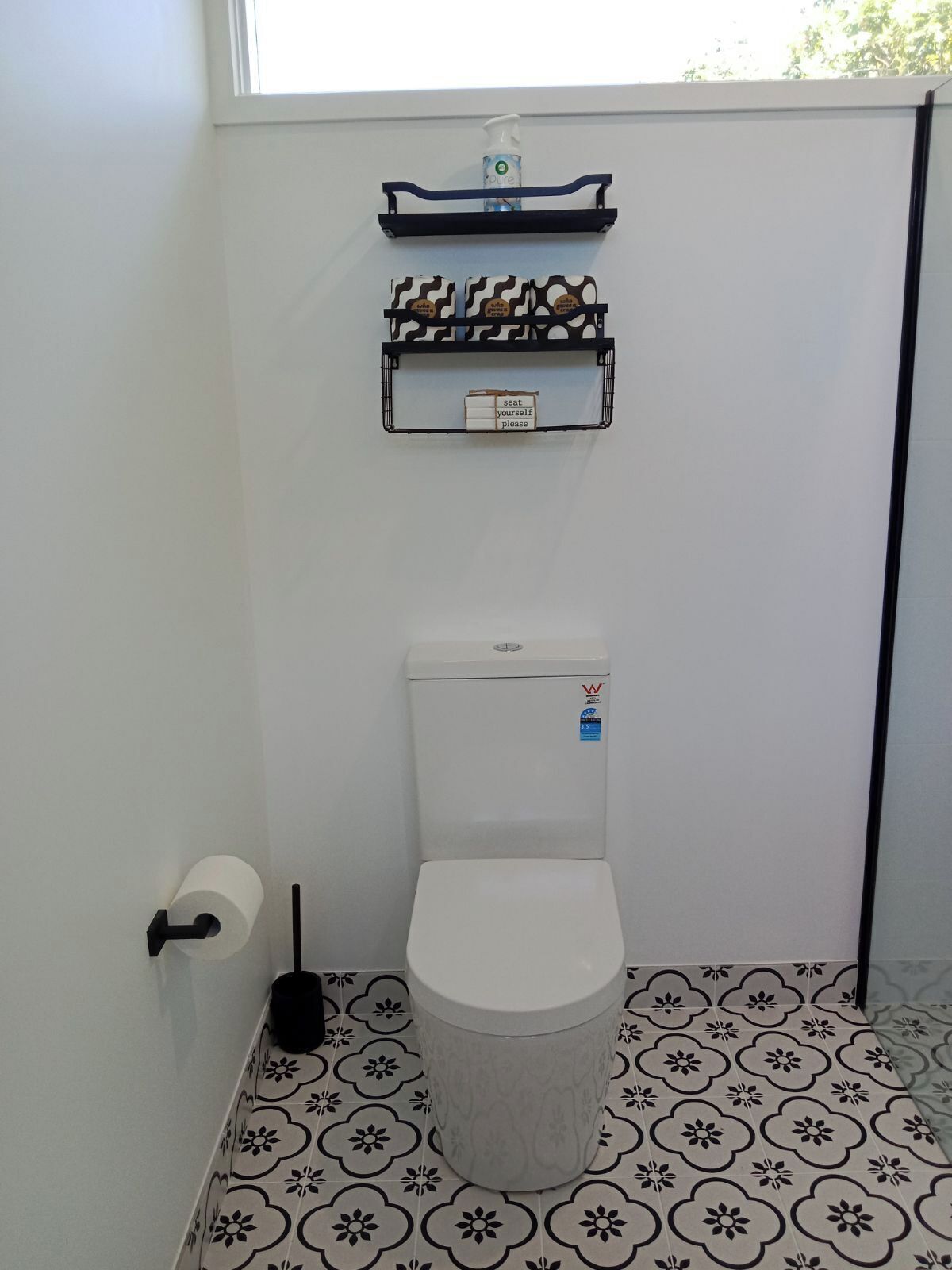 A small bathroom with a toilet, a toilet paper holder, a hand dryer, and a shelf with toiletries.
