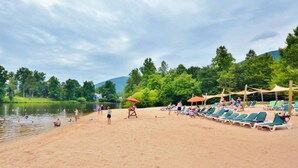 Une plage bordée de rangées de chaises longues et de parasols, un lac paisible et, au loin, une colline boisée.