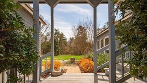Un espace extérieur abrité, doté d’une terrasse en bois, d’un panier pour chien et offrant une vue sur une cour verdoyante avec des arbres.