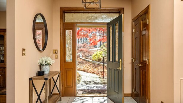 A hallway with a wooden door, a mirror, and a small table with a vase of flowers. - The Wintergreen Treehouse (Nellysford)