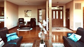 A spacious living room with a wooden floor, two black leather sofas with blue cushions, a coffee table, and a potted orchid plant. - The Wintergreen Treehouse (Nellysford)