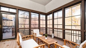 A sunroom with large windows, wooden furniture, and a view of trees. - The Wintergreen Treehouse (Nellysford)