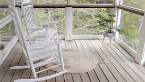 Een houten terras met witte schommelstoelen en een potplant.