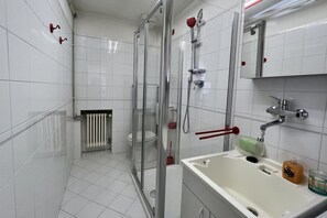 Une salle de bain moderne avec une douche à parois de verre, un lavabo blanc doté d’un distributeur de savon et des toilettes.
