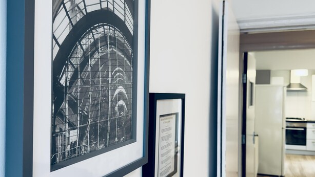 A hallway with framed architectural drawings on the wall, leading to a kitchen area. - Stylish House in Sheffield (Sheffield)