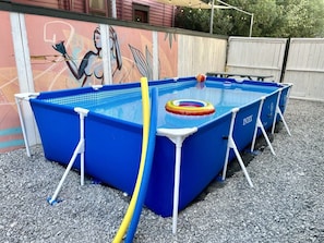 A blue above-ground pool with a ladder, surrounded by gravel, and a mural on the wall behind. - Claiborne Guest House w/pool by Historic Getaways (New Orleans)