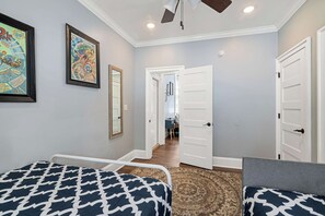 A hotel room with two beds, a ceiling fan, a framed artwork, and a hallway leading to another room. - Claiborne Guest House w/pool by Historic Getaways (New Orleans)