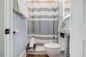 A bathroom with a striped shower curtain, a toilet, a sink, and a towel rack. - Claiborne Guest House w/pool by Historic Getaways (New Orleans)