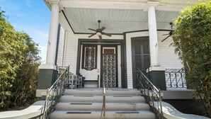 A two-story building with a porch, a ceiling fan, and a staircase leading to the entrance.