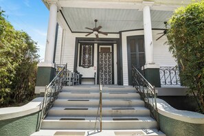 A two-story building with a porch, a ceiling fan, and a staircase leading to the entrance. - Claiborne Guest House w/pool by Historic Getaways (New Orleans)
