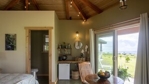 Una habitación acogedora con cama, una mesa de comedor con un cuenco de fruta, una pequeña kitchenette y un amplio ventanal corredero que da a una vista panorámica del exterior.