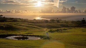 Un paisaje con colinas onduladas, un pequeño estanque y una masa de agua distante bajo un cielo al atardecer.