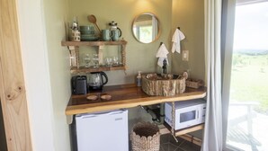 Una cocina compacta con cubierta de madera, horno microondas integrado, cafetera y pileta de madera rústica.