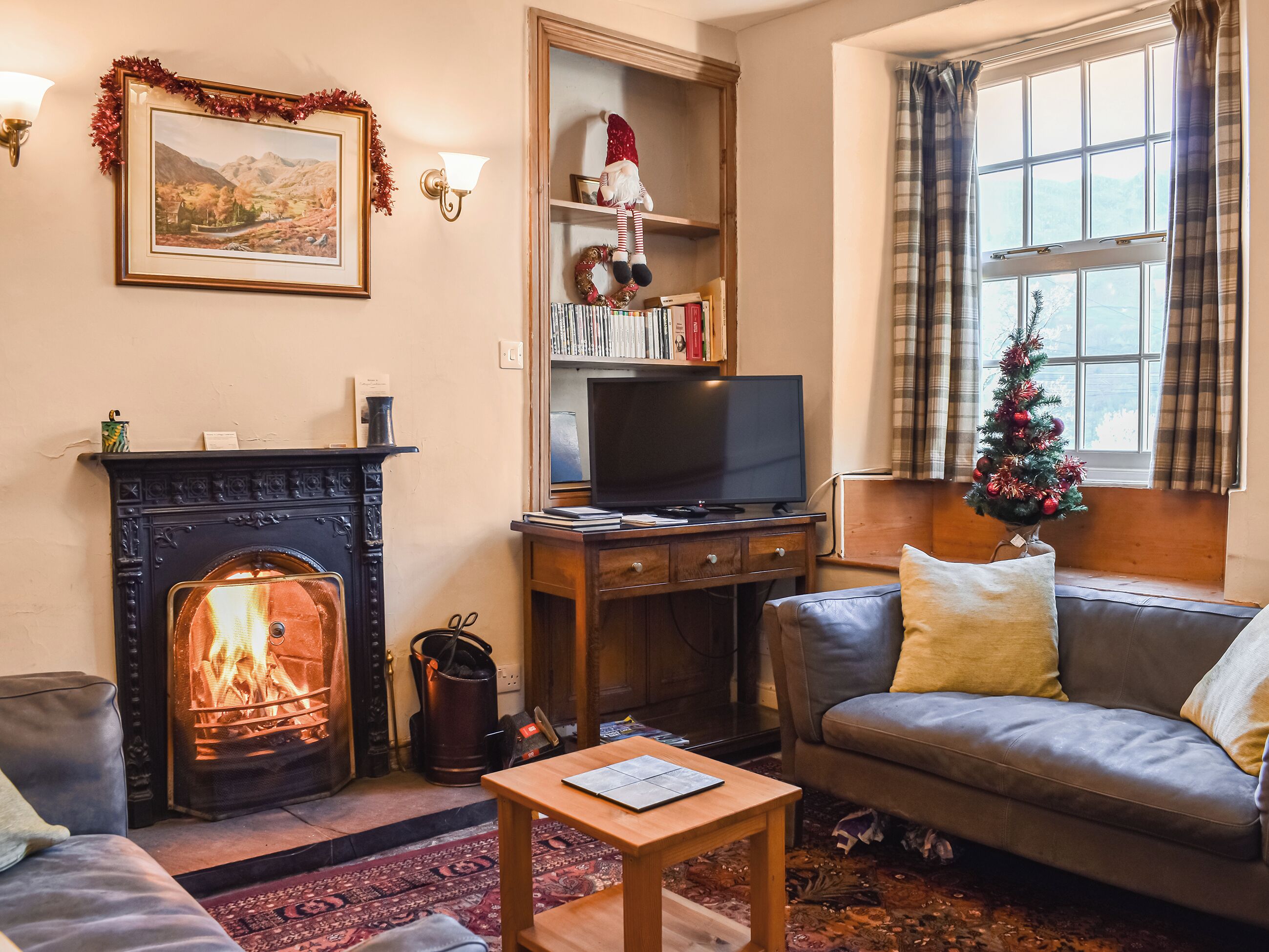 A cozy living room with a fireplace, a television, a bookshelf, and a Christmas tree.