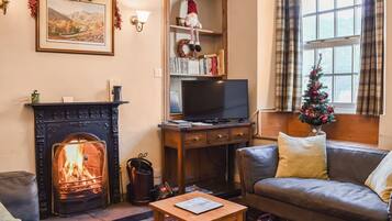 A cozy living room with a fireplace, a television, a bookshelf, and a Christmas tree.