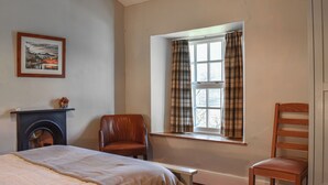 Een kamer met een bed, een open haard, een raam met gordijnen, een stoel en een houten stoel.