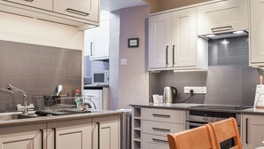 Een moderne keuken met grijze kastjes, een roestvrijstalen spoelbak en een eethoek met een houten stoel en tafel.
