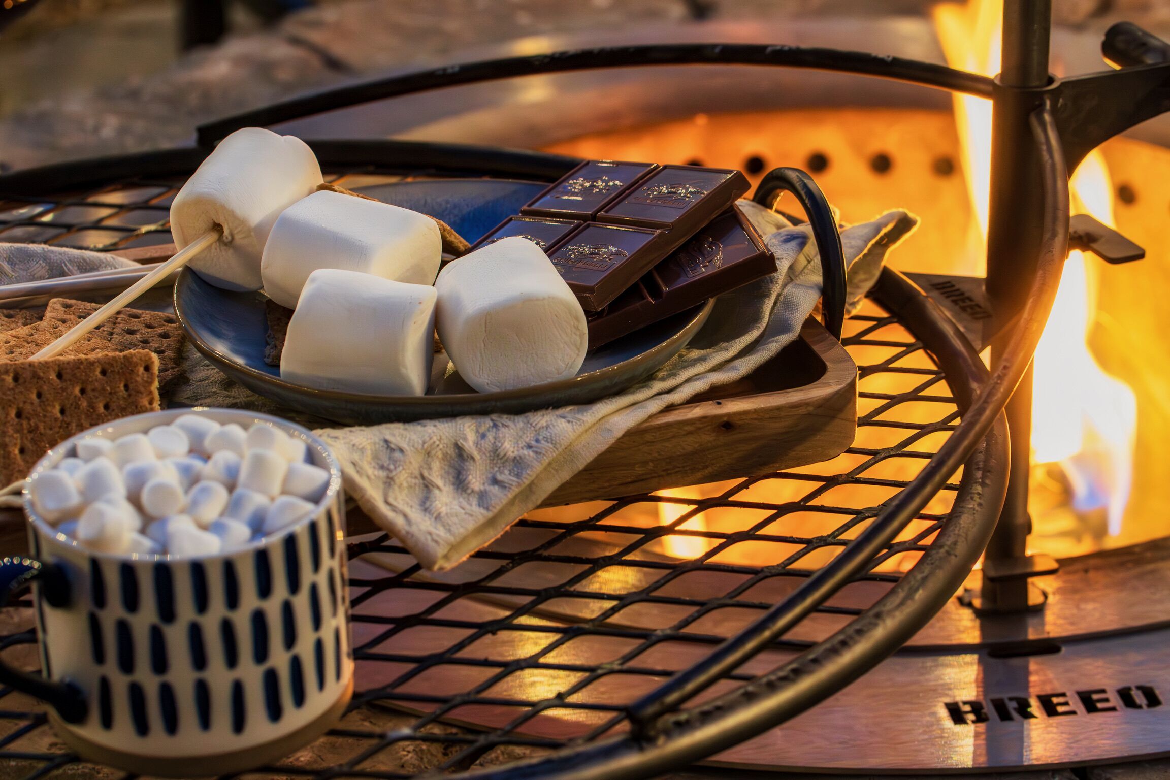 Ein Lagerfeuer mit Marshmallows, Schokolade und einer Tasse Marshmallows auf einer Metallplatte.