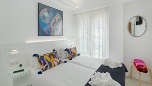 A hotel room with a bed, a bedside table with a remote control, a mirror, and a window with curtains.