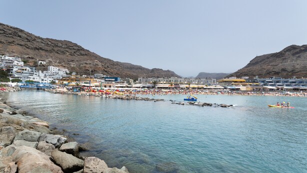 A coastal town with buildings along the waterfront, clear blue water, and rocky terrain.