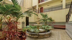 A courtyard with a fountain, potted plants, a bench, and a tiled floor.
