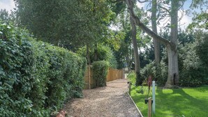 Un sentier de jardin bordé d’une clôture en bois, entouré d’un feuillage dense et d’arbres.