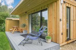 Een houten terras met een picknicktafel en loungestoelen.