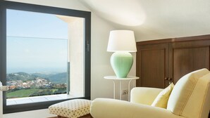 A room with a view of a town, a green vase on a small table, a white sofa, and a wooden cabinet.