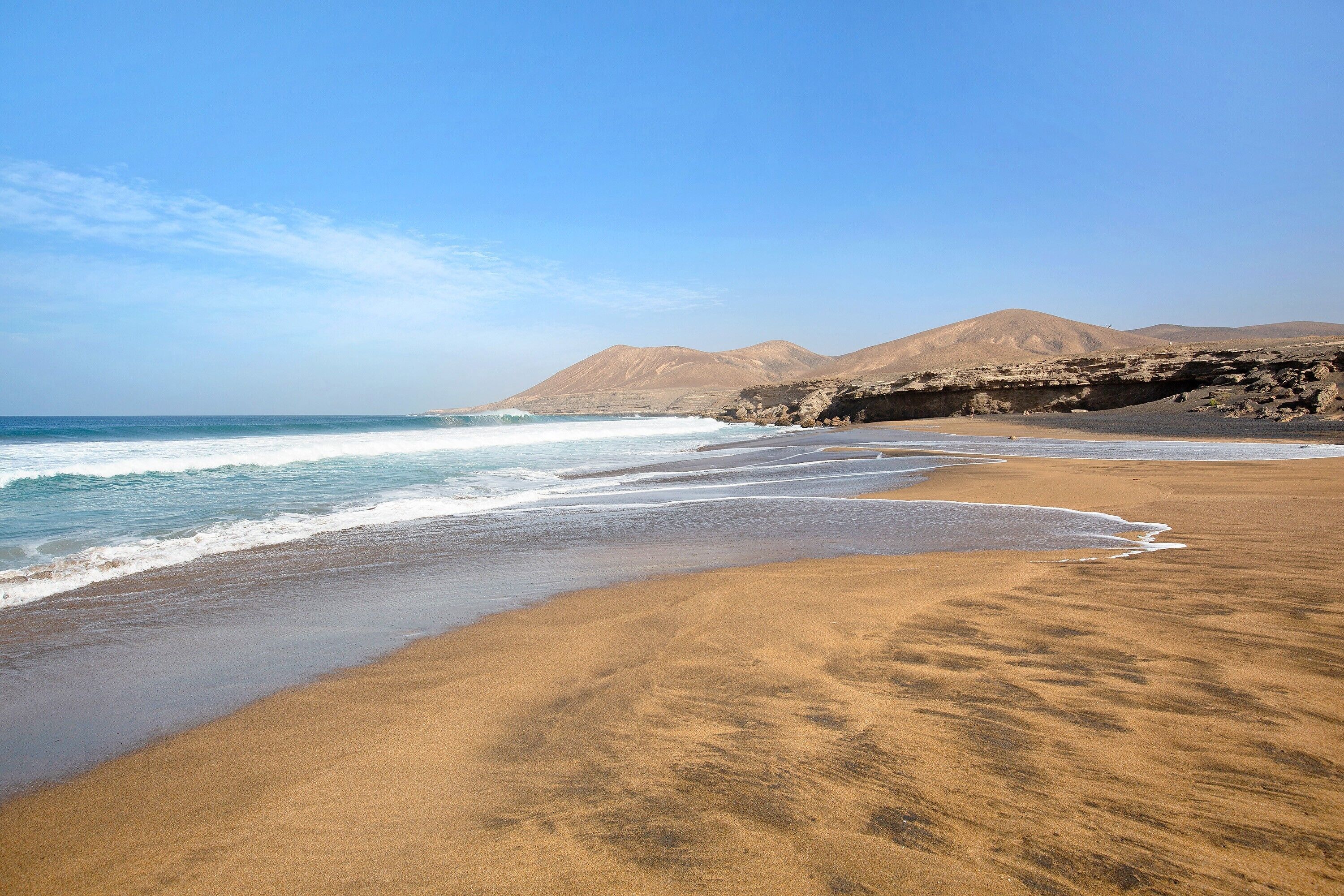 A beach with a sandy shore, waves, and distant mountains.