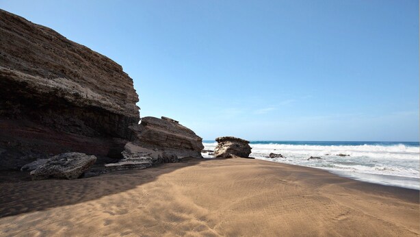 A beach with a rocky cliff and ocean waves.