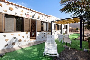 Un bâtiment doté d’une façade en pierre, d’un patio couvert avec une table et des chaises, et d’un fauteuil de jardin blanc.
