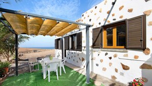 A patio with a table and chairs, a covered area, and a view of the sea.