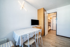 A room with a wooden floor, a white table with a patterned tablecloth, a flat-screen TV, and a wooden cabinet.