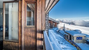 A wooden cabin with a glass door, a balcony with snow, and a view of a snowy mountain landscape. - Studio Apartment 'Samoens 1600' with Balcony (Samoëns)