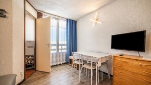 A room with a dining table, chairs, a TV, a wooden dresser, and a wardrobe. - Studio Apartment 'Samoens 1600' with Balcony (Samoëns)