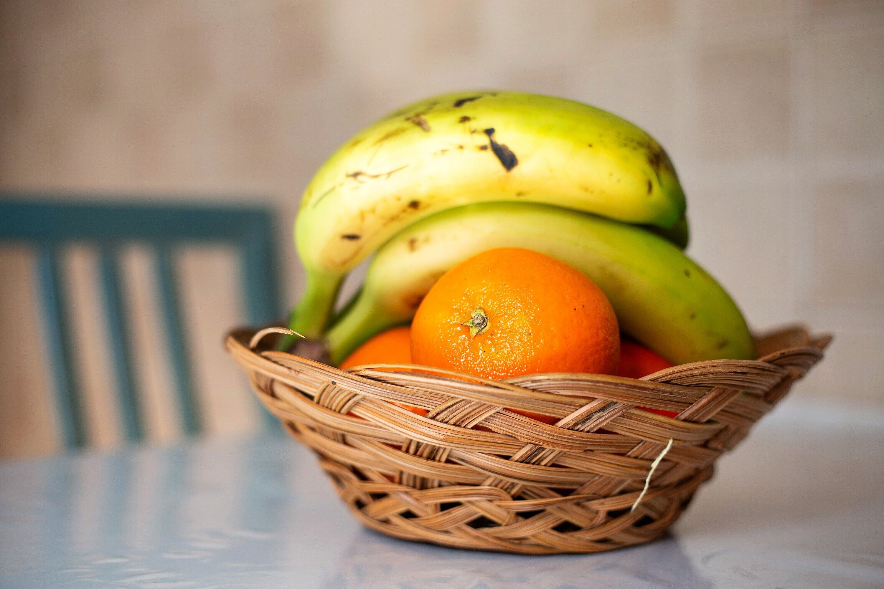 Un cesto di vimini con banane e un'arancia su un tavolo.