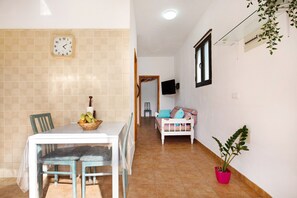 A hallway with a dining table, chairs, a sofa, a potted plant, and a wall clock. - Vacation Home 'Apartamento La Solapa' with Mountain View, Shared Garden and Wi-Fi (PAJARA)