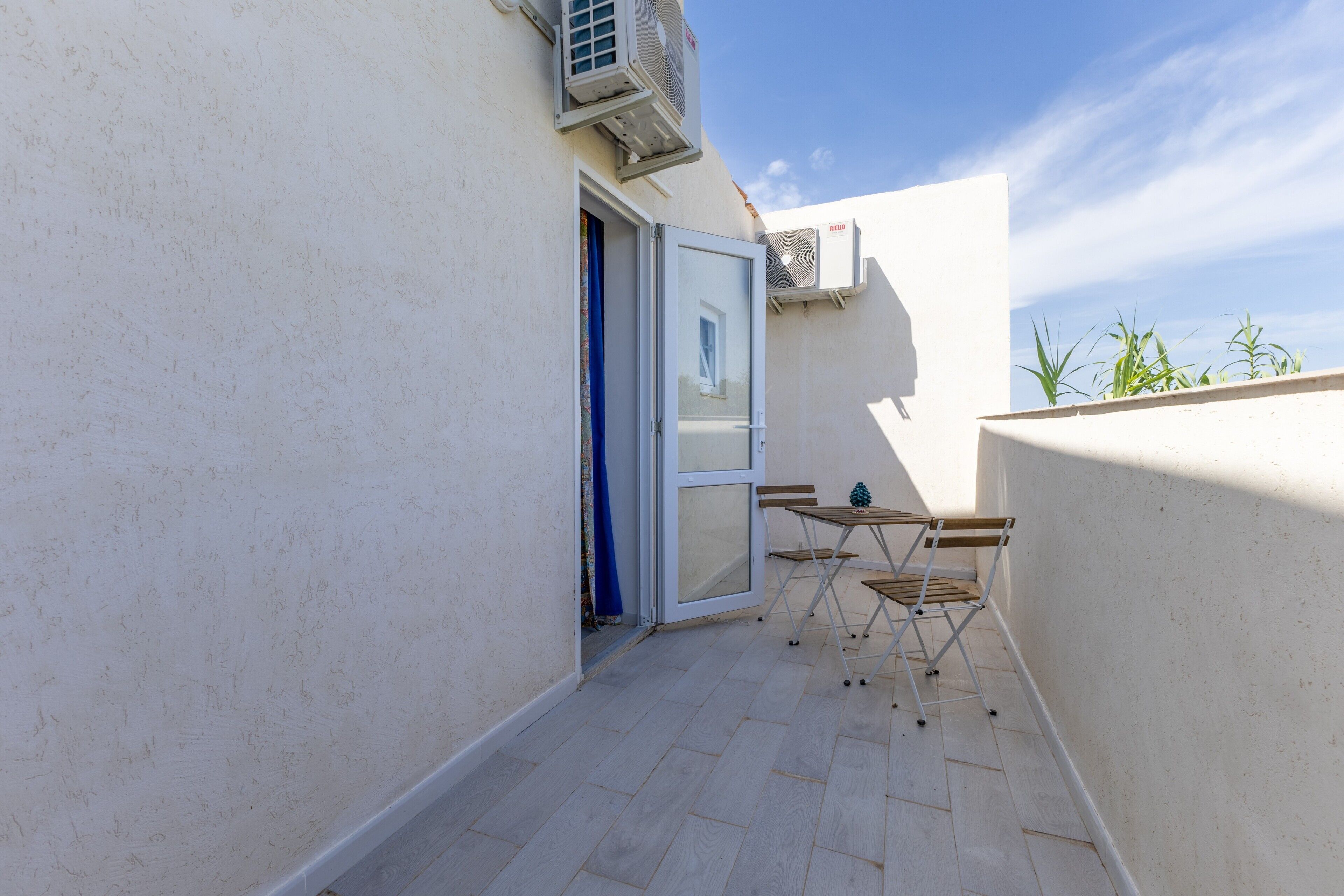 Un balcon extérieur avec un mur blanc, une porte coulissante et une petite table avec des chaises.